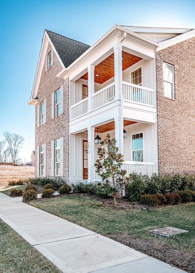 view of front of house featuring a balcony, a shingled roof, board and batten siding, and brick siding