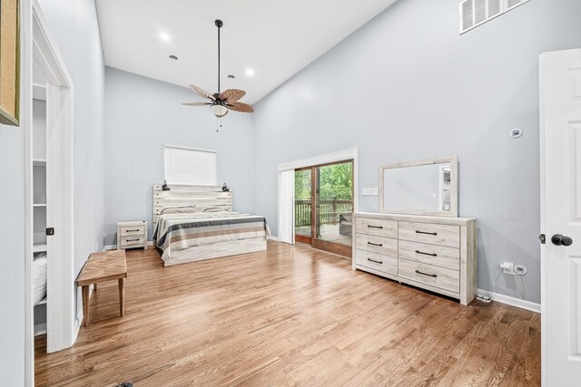 bedroom with baseboards, visible vents, wood finished floors, access to outside, and a high ceiling