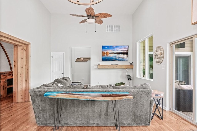 living room with a towering ceiling, ceiling fan, visible vents, and wood finished floors