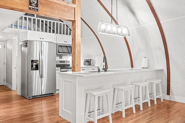 kitchen with stainless steel appliances, a kitchen breakfast bar, white cabinets, and light wood finished floors