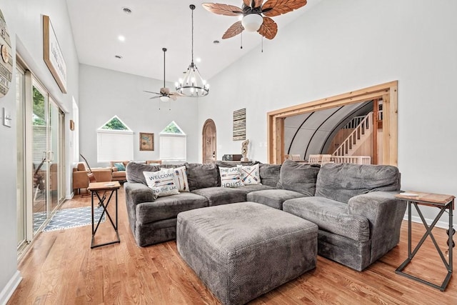 living area featuring arched walkways, ceiling fan with notable chandelier, a towering ceiling, stairway, and light wood-type flooring