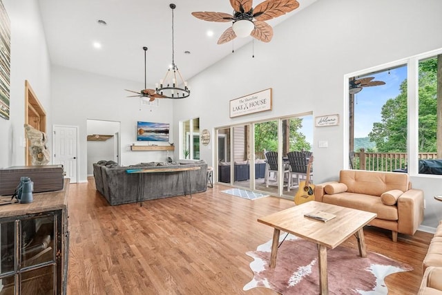 living room with ceiling fan with notable chandelier, recessed lighting, a towering ceiling, and light wood-style floors