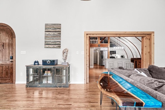 bedroom featuring arched walkways, baseboards, wood finished floors, and stainless steel fridge with ice dispenser