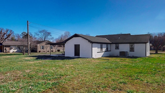 back of property with a carport, stucco siding, a lawn, and central air condition unit