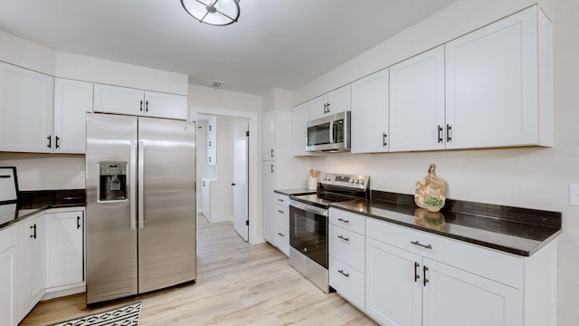 kitchen featuring appliances with stainless steel finishes, dark countertops, white cabinetry, and light wood finished floors