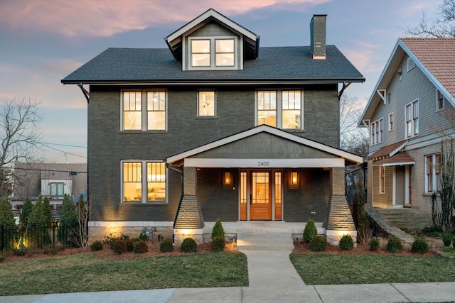 american foursquare style home featuring covered porch, brick siding, and a chimney