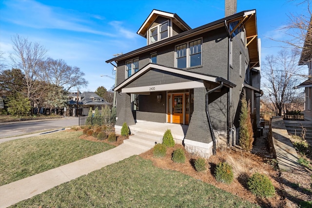 american foursquare style home with brick siding, a chimney, a porch, and a front lawn