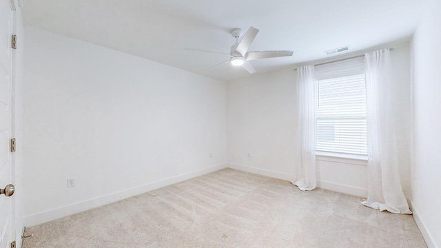 empty room featuring a ceiling fan, light colored carpet, visible vents, and baseboards