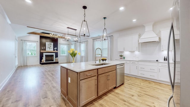 kitchen with light wood finished floors, a fireplace with raised hearth, appliances with stainless steel finishes, premium range hood, and a sink