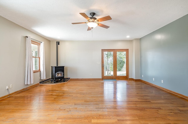 unfurnished living room with a wood stove, light wood finished floors, baseboards, and a ceiling fan