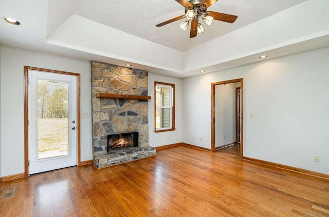 unfurnished living room with visible vents, a fireplace, a tray ceiling, and light wood-style flooring