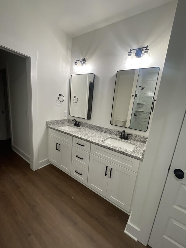 bathroom with a shower, double vanity, a sink, and wood finished floors