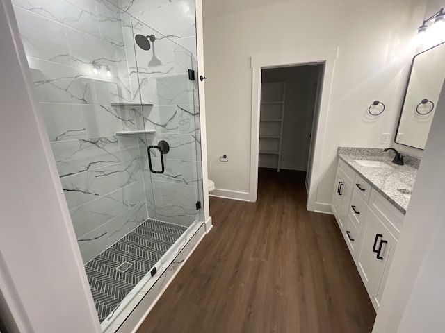 bathroom with double vanity, a marble finish shower, baseboards, wood finished floors, and a sink