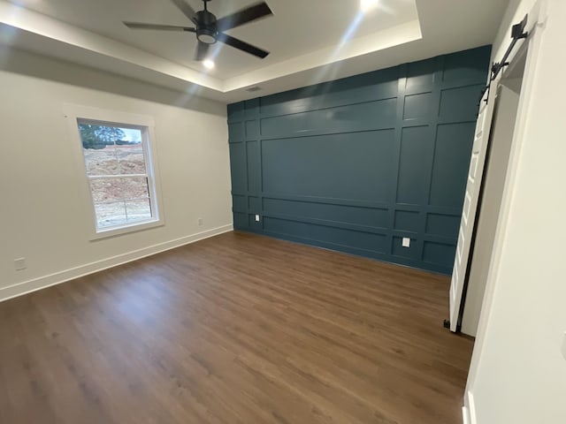 unfurnished bedroom with a tray ceiling, a barn door, and a decorative wall