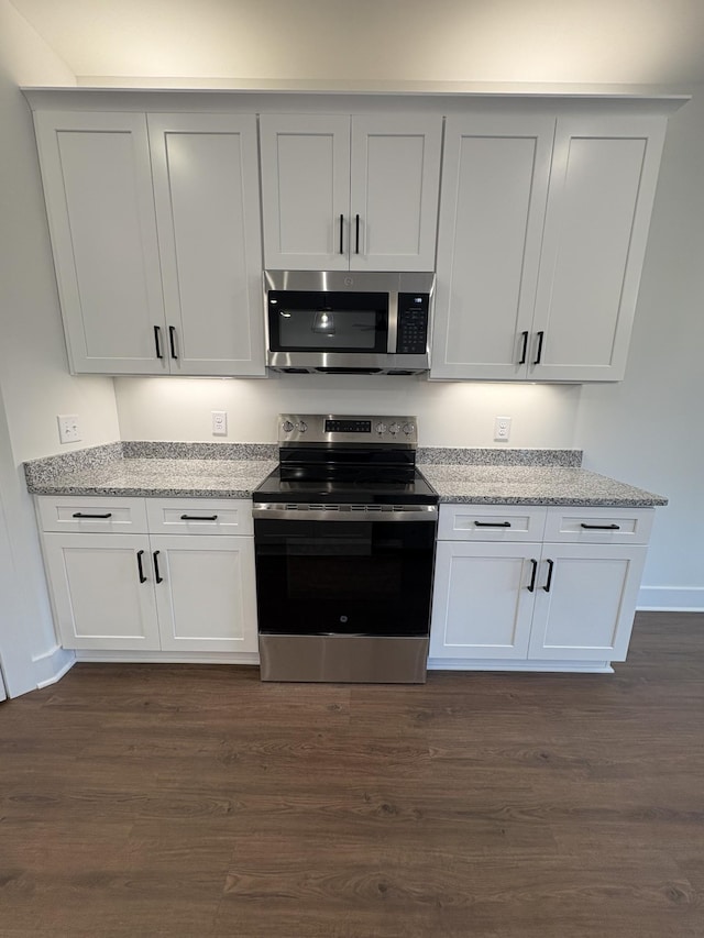 kitchen with appliances with stainless steel finishes, light stone counters, and dark wood-style floors