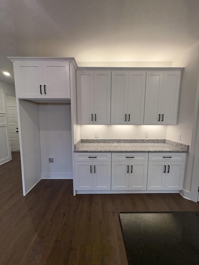 kitchen featuring white cabinetry, dark wood finished floors, baseboards, and light stone countertops