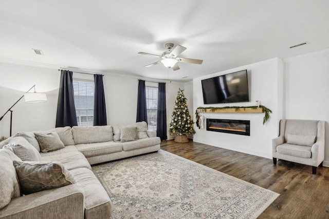 living room featuring visible vents, dark wood-style flooring, crown molding, and a glass covered fireplace