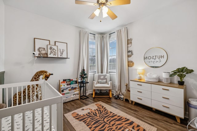 bedroom featuring dark wood-type flooring, ceiling fan, and a crib