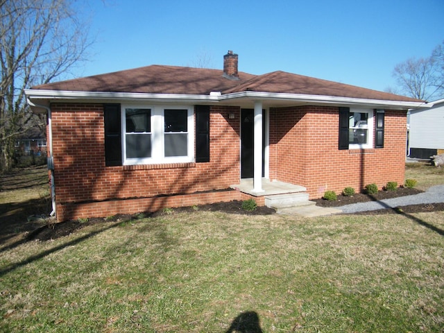 view of front of home with a front yard, a chimney, and brick siding