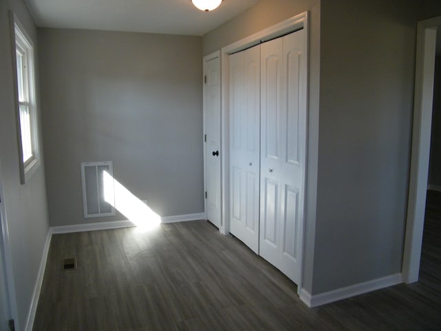 unfurnished bedroom with dark wood-style floors, baseboards, visible vents, and a closet