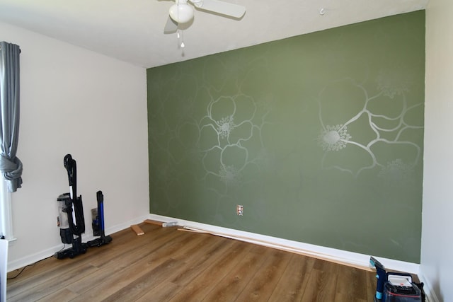 empty room featuring an accent wall, wood finished floors, a ceiling fan, and baseboards