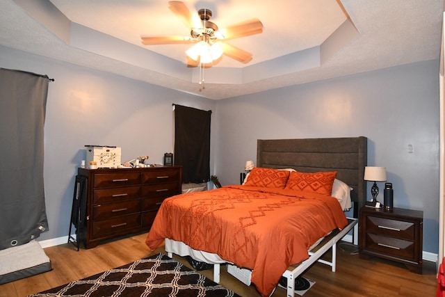 bedroom featuring a ceiling fan, a raised ceiling, baseboards, and wood finished floors