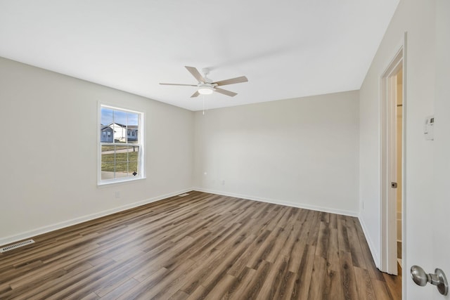 spare room featuring dark wood-style floors, ceiling fan, visible vents, and baseboards