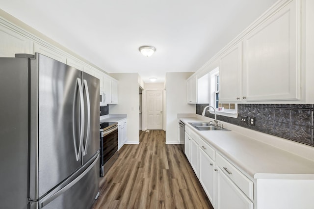 kitchen with appliances with stainless steel finishes, wood finished floors, a sink, white cabinetry, and backsplash