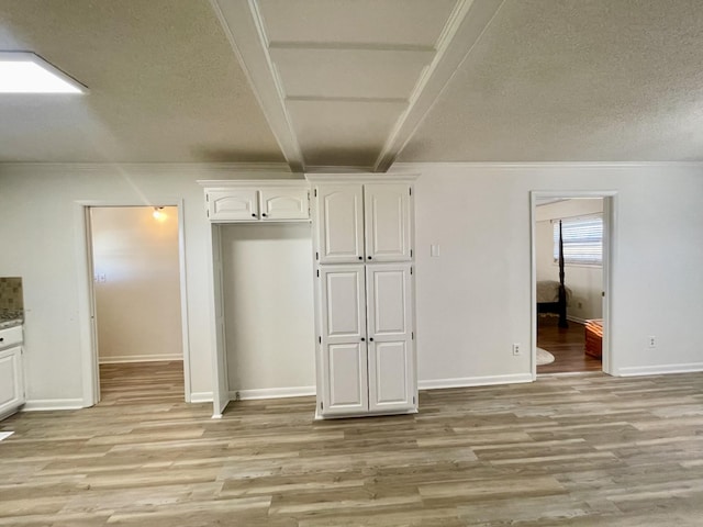 interior space featuring light wood finished floors, ornamental molding, white cabinets, and beam ceiling