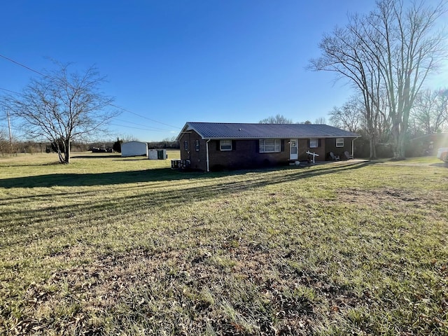 view of front of property featuring a front yard, brick siding, metal roof, and an outdoor structure