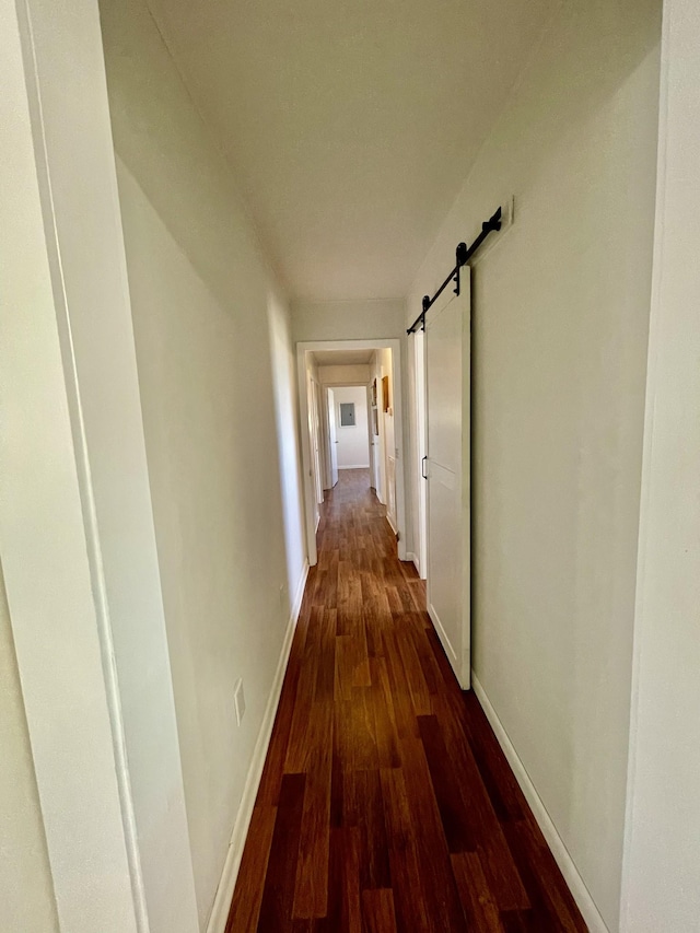 corridor featuring a barn door, baseboards, and dark wood-type flooring