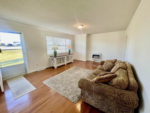 living area with a textured ceiling, wood finished floors, visible vents, and heating unit