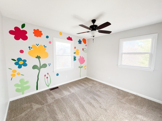 carpeted empty room with a healthy amount of sunlight, baseboards, visible vents, and a ceiling fan