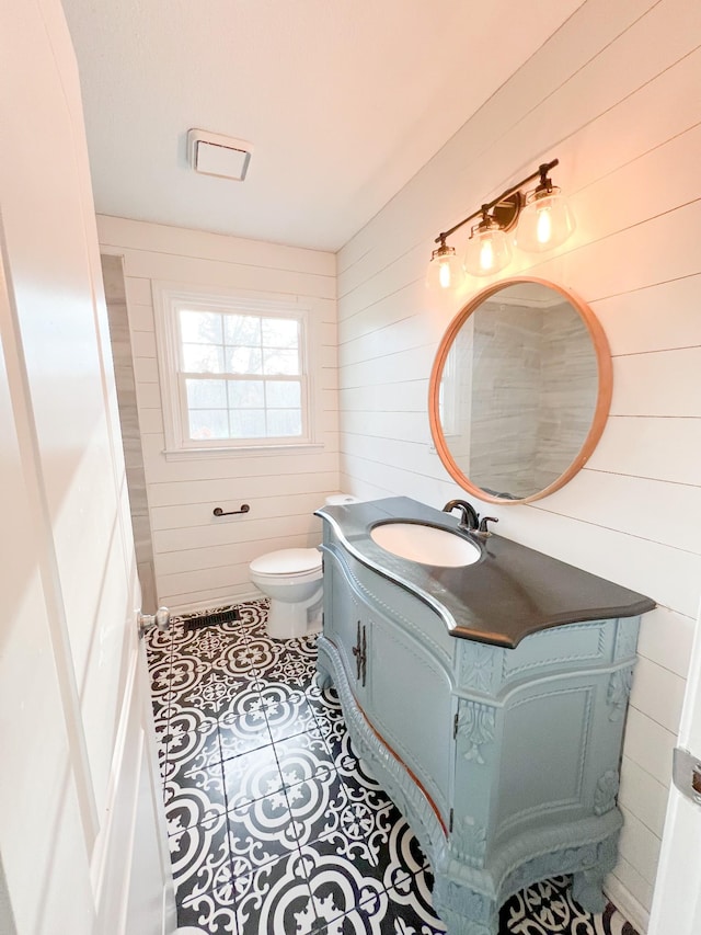 bathroom with toilet, wooden walls, vanity, and tile patterned floors