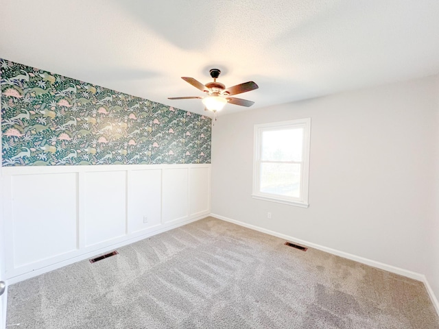 carpeted spare room with wainscoting, visible vents, a textured ceiling, and wallpapered walls