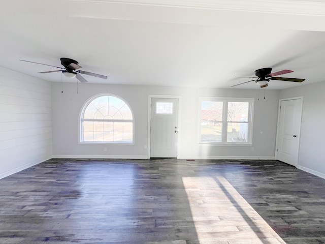 unfurnished living room featuring dark wood-style flooring, a ceiling fan, and baseboards