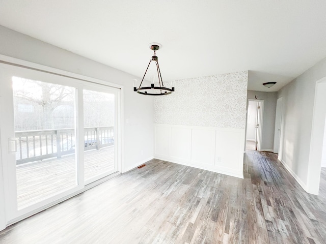 unfurnished dining area featuring a chandelier, wood finished floors, baseboards, wainscoting, and wallpapered walls