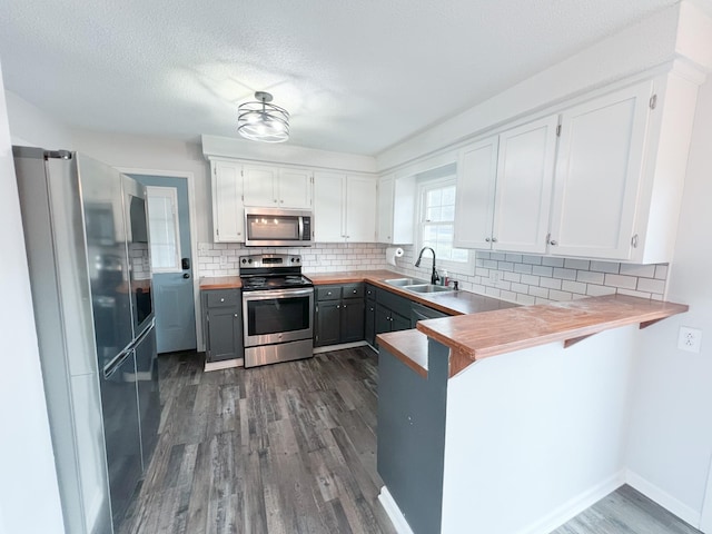 kitchen with tasteful backsplash, appliances with stainless steel finishes, dark wood-type flooring, a peninsula, and a sink