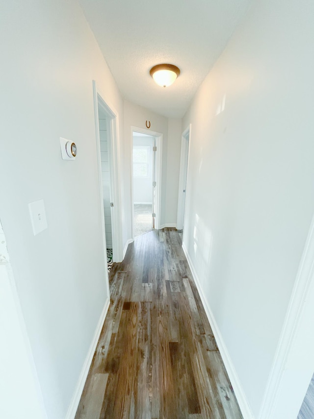 hall with a textured ceiling, wood finished floors, and baseboards