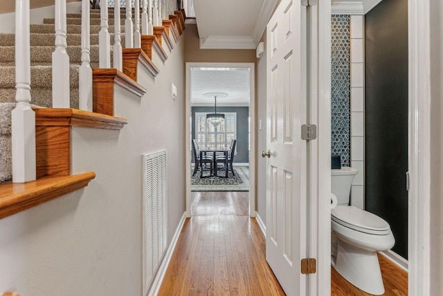 corridor with baseboards, visible vents, wood finished floors, stairs, and crown molding