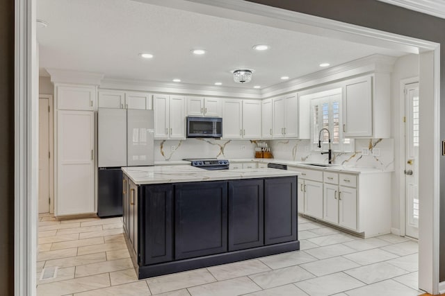 kitchen with a center island, stainless steel microwave, freestanding refrigerator, white cabinets, and a sink