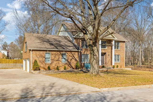 neoclassical / greek revival house featuring concrete driveway, brick siding, fence, and a front lawn