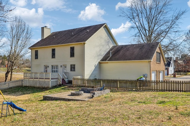 rear view of property with a chimney, a lawn, fence, a deck, and a fire pit