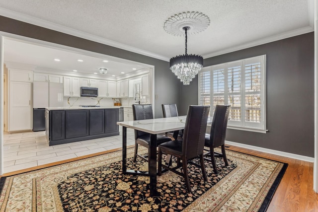 dining room featuring baseboards, a textured ceiling, crown molding, light wood-style floors, and a notable chandelier