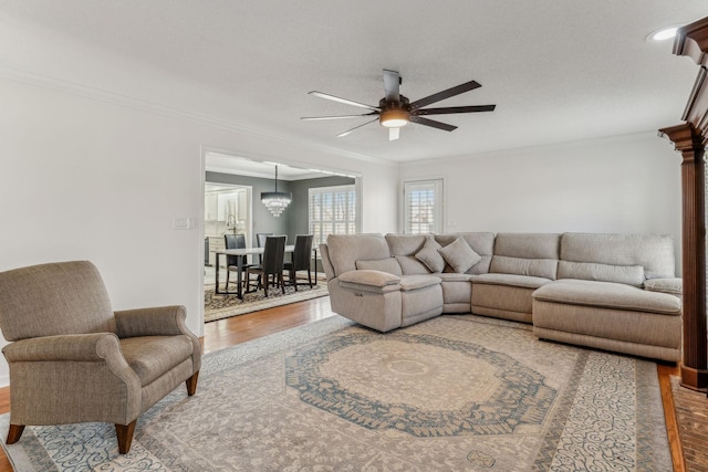 living area with ceiling fan with notable chandelier, crown molding, and wood finished floors