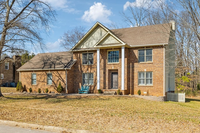 neoclassical / greek revival house with a front yard, brick siding, and a chimney