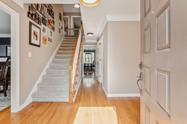 entrance foyer with light wood finished floors, baseboards, stairway, and crown molding