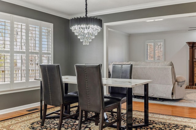 dining space featuring baseboards, a chandelier, crown molding, and wood finished floors