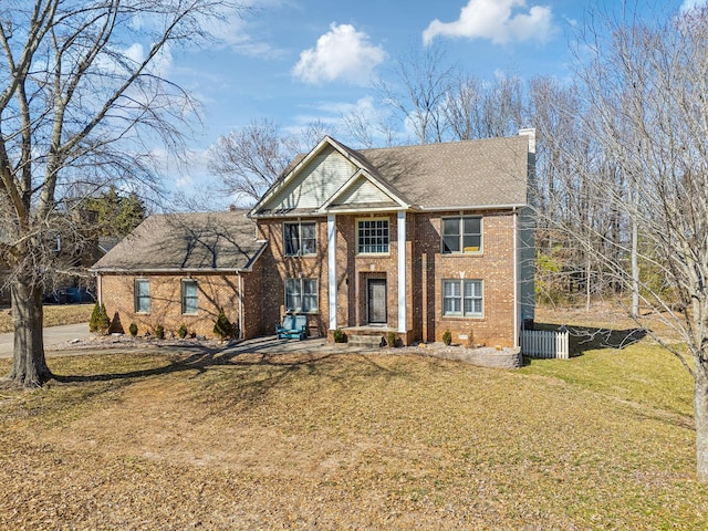 neoclassical / greek revival house featuring brick siding, a chimney, and a front lawn