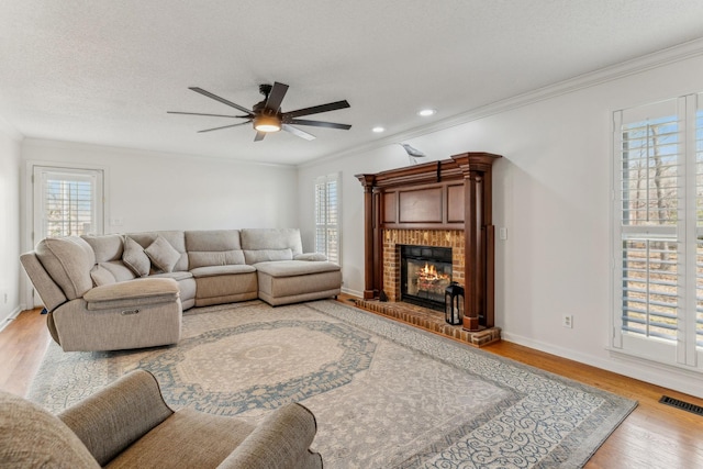 living area featuring light wood finished floors, visible vents, ornamental molding, a textured ceiling, and a brick fireplace